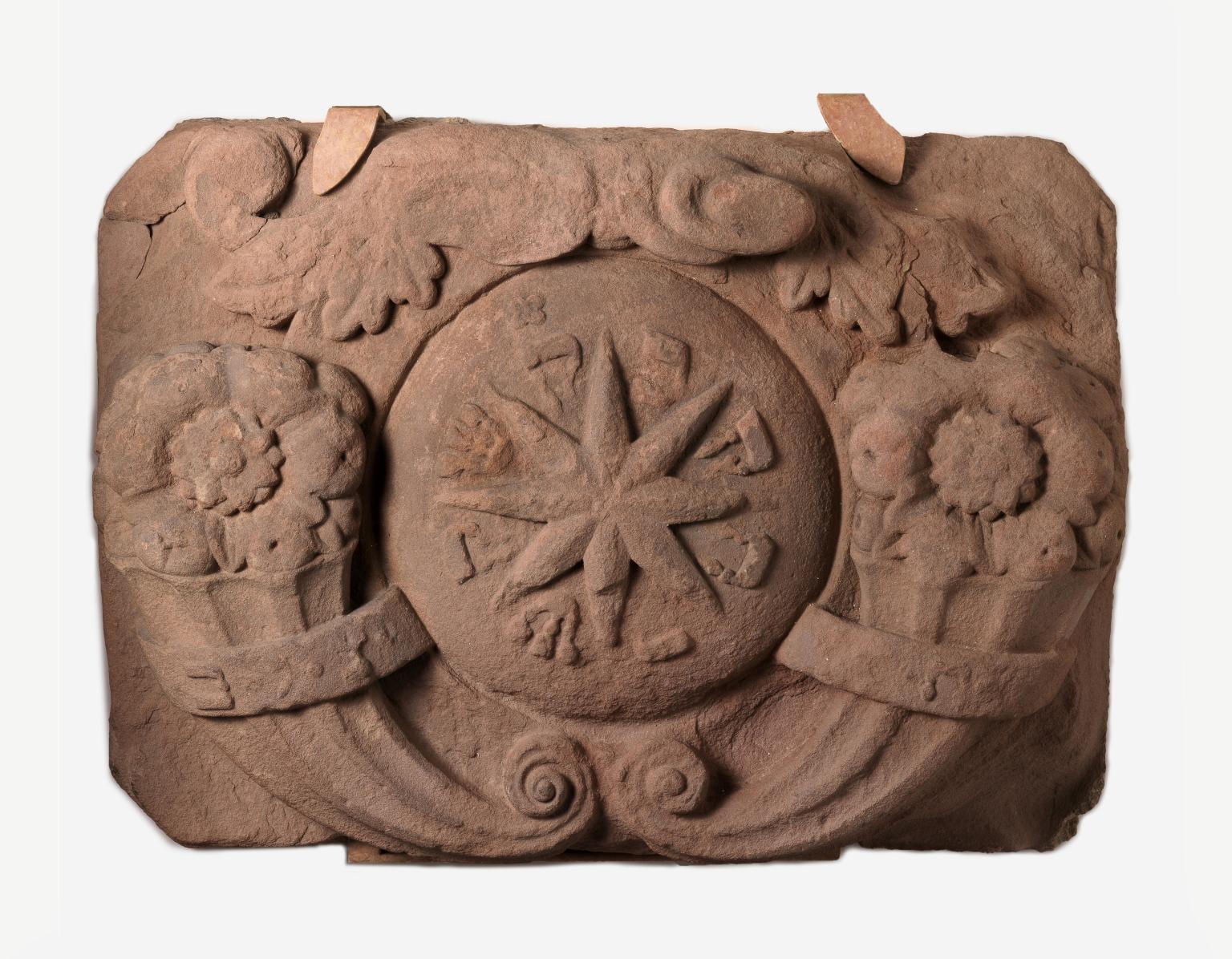 Stone with carving of star in center and flowers on either side.