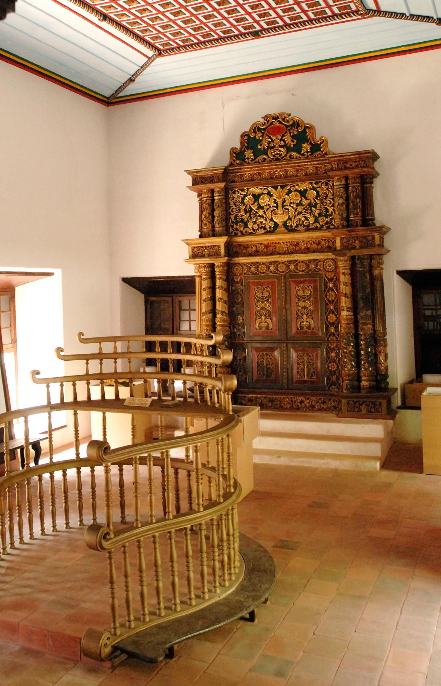 Photograph of room with raised platform with railings in center and carved wooden Torah chamber on back wall.  