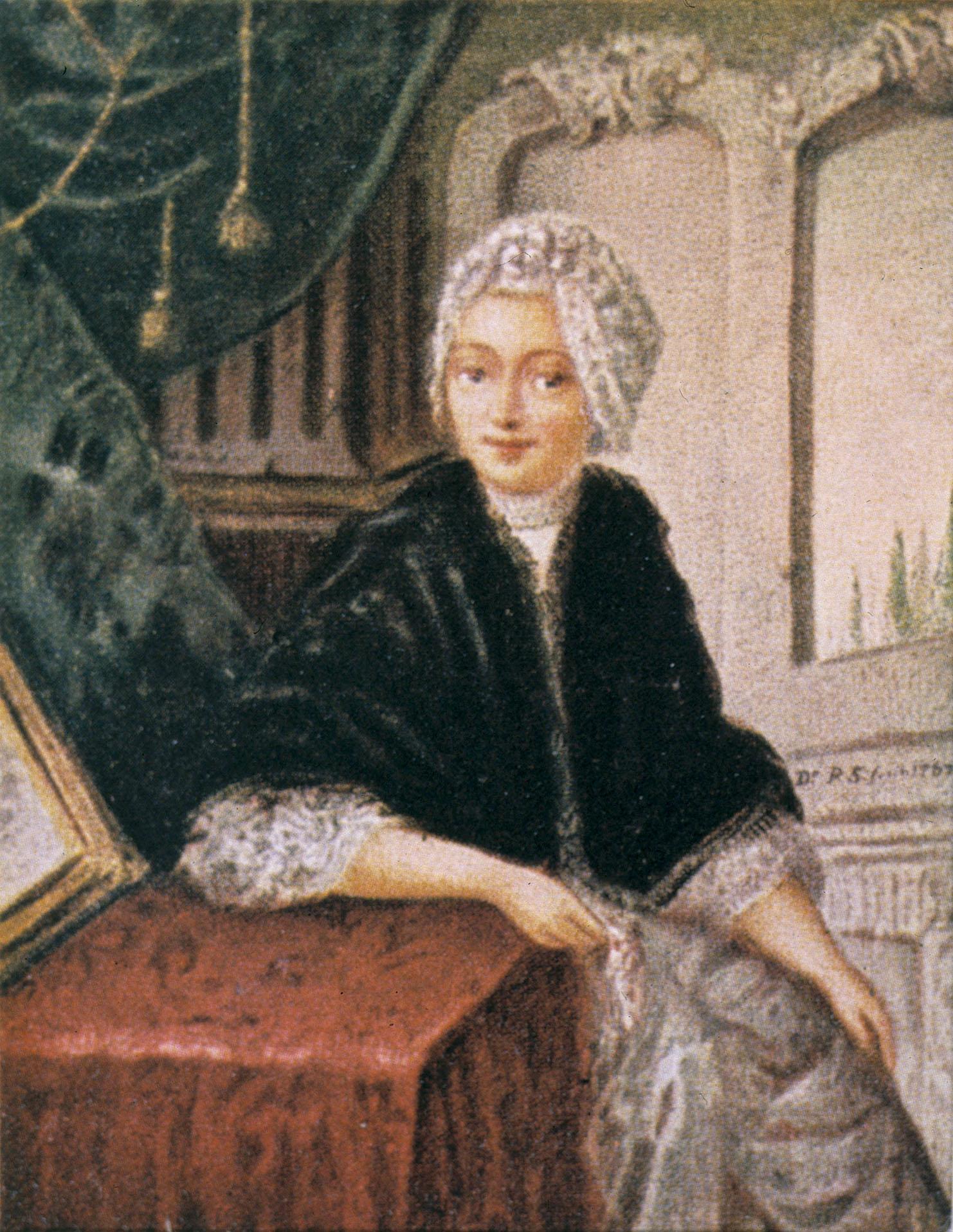 Image of seated woman in shawl with arm resting on a table with tablecloth.