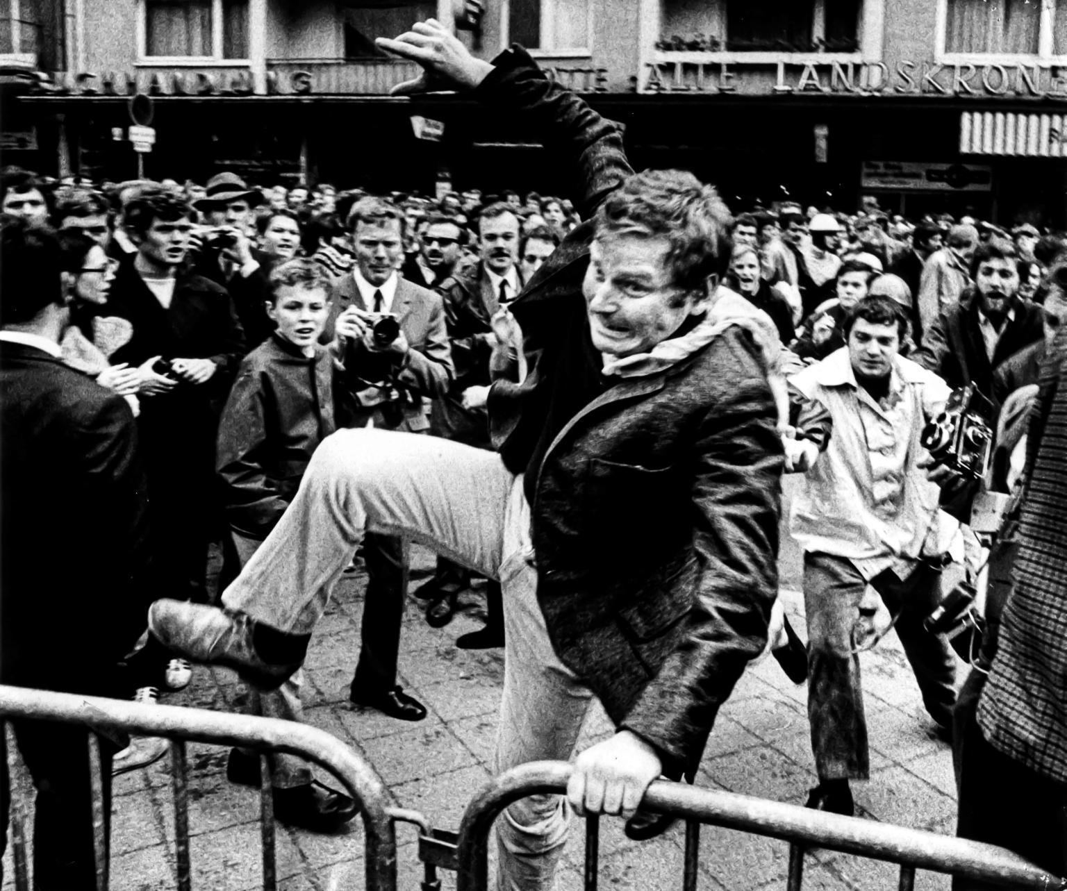 Photograph of a man jumping barricade in front of crowd of people.
