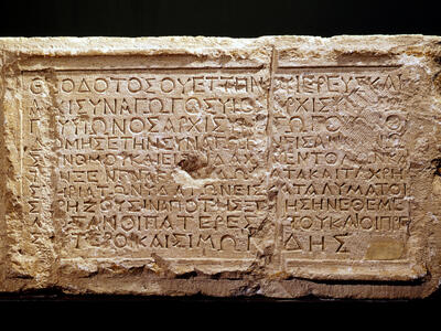 An ancient rectangular stone tablet engraved with Greek text, featuring clear, deeply carved letters and some signs of wear and erosion on the surface.