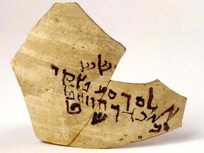 A broken piece of pottery with ancient Hebrew script written in black ink across its surface.
