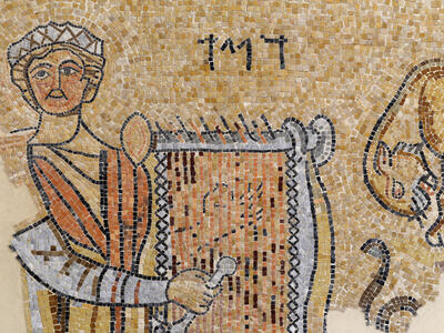 Ancient mosaic showing a person in a robe holding a lyre, with Hebrew letters above and part of an animal figure on the right side.