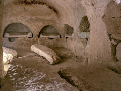 Ancient stone chamber with arched alcoves carved into the walls and rectangular stone slabs on the ground.