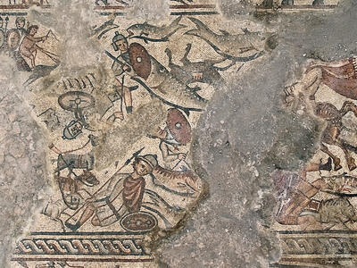 Ancient mosaic depicting armored figures, horses, and combat scenes; some parts of the artwork are missing or damaged, revealing patches of bare stone.