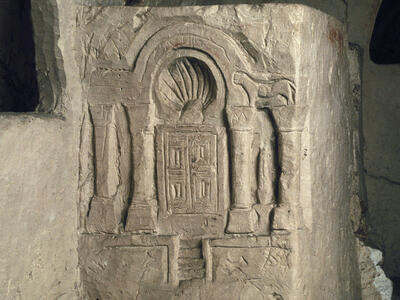 Stone carving of an ornate structure with two pairs of columns, an arched top, intricate door panels, and steps leading up, etched into a rough stone surface.