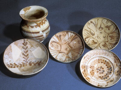 Five pieces of pottery are displayed on a flat surface: one small jar and four shallow bowls, all decorated with intricate brown geometric and floral patterns.