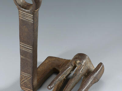 A metal object with a vertical handle featuring etched lines, attached to a flat base with five prongs at the end resembling a claw.