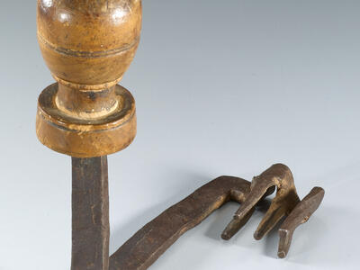 An object with a round wooden handle and a metal shaft ending in prongs resembling a claw.