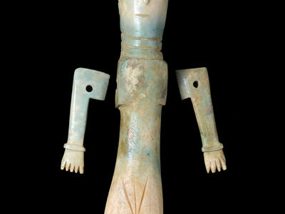 A carved bone figurine with a long body, stylized arms, a detailed headdress, and simple facial features.