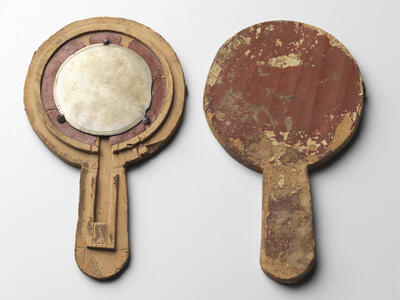 Two ancient wooden hand mirrors with round shapes and handles. The mirror on the left has a reflective circular metal surface; both show signs of heavy wear, scratches, and peeling surfaces.