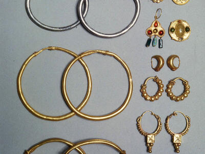 A collection of ancient jewelry, including rings, earrings, and bangles in various sizes and designs, made of gold and silver, some with gemstones.