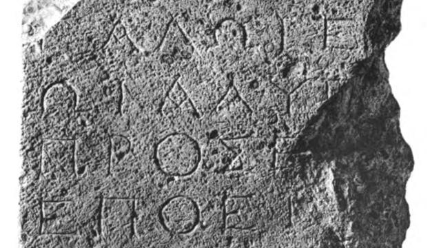 A stone fragment inscribed with ancient Greek text in several lines. The edges are irregular and broken.