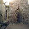 Photo of a stone room with an arched doorway, stone benches and columns, and a stairway.
