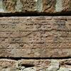 Photo of a stone plaque with weathered, engraved Hebrew text, mounted into a brick wall.