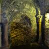 Photo of a stone archway framed by columns and leading to a descending passageway made of rough stone.