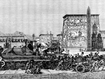 Israel in Egypt Enslaved people pull a cart bearing a sphynx past monumental Egyptian buildings decorated in heiroglyphs.