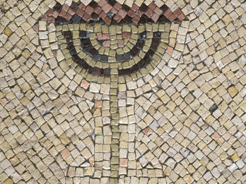 A stone mosaic of a menorah, in shades of tan, red, blue, and black
