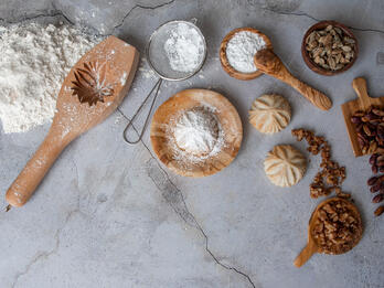 Two white, flower-shaped cookies surrounded by utensils and ingredients.