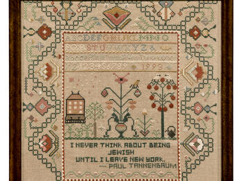 Needlework in a frame with a border of designs, the alphabet and numbers in the center, and text at the bottom.