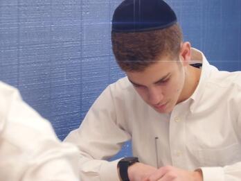 Thumbnail photo of yeshiva student leaned over a desk writing.