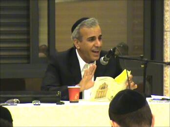 Thumbnail photo of orthodox man holding a book and speaking into a microphone.