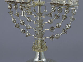 Hanukkah Lamp Eight-branched candelabrum with figure on top brandishing sword.