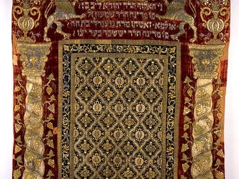 Torah Ark Curtain Cloth with embroidered columns on either side, pattern in the middle, and Hebrew text between two lions and crown on top.