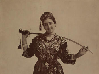 Photograph of figure holding sword behind her neck.