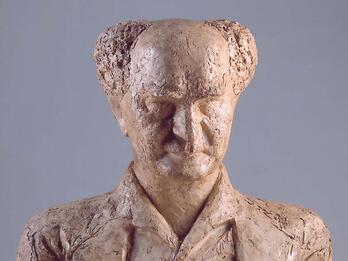 Bust sculpture of an elderly man with central bald spot facing viewer.