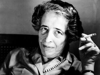 Portrait photograph of a woman looking at the camera and holding up a cigarette in her left hand.