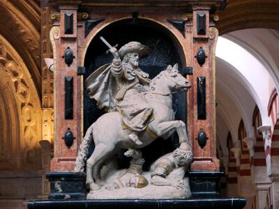 Photo of stone statue with gold trim of a man holding up a sword riding a horse that is trampling soldiers, surrounded by ornate decorated arches and features.