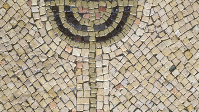A stone mosaic of a menorah, in shades of tan, red, blue, and black
