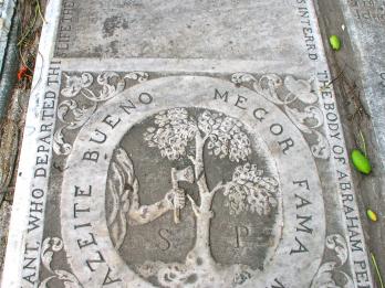 Tombstone with Latin inscription on top half and illustration below of axe chopping tree in half, surrounded by English words around perimeter of stone.