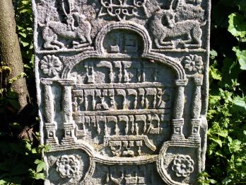 Tombstone with Hebrew inscription in geometric shape with columns and animals surrounding.