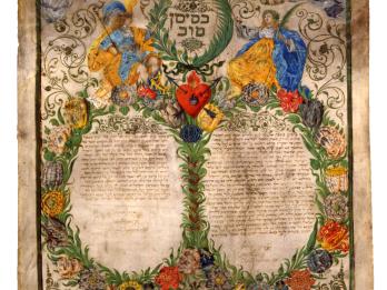 Page of Aramaic text arranged in two columns surrounded by foliage and two angelic figures at top. 