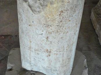 Cylindrical tombstone with Hebrew on top, sitting on decorative base.