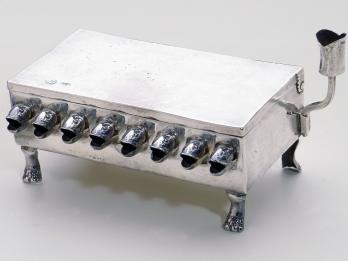 Silver rectangular lamp with fish-head spouts for the oil and paw-shaped feet.