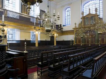 Photograph of room with wooden pews, ornate Torah ark in far wall, and second story balcony.