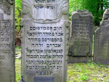 Tombstone of relief of open books, Hebrew inscriptions, and two lanterns on ground in front. 