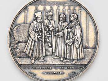 Silver medal depicting four men talking.
