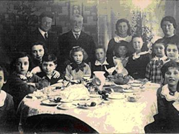 Photograph of many people sitting around a set table and looking at the camera. 