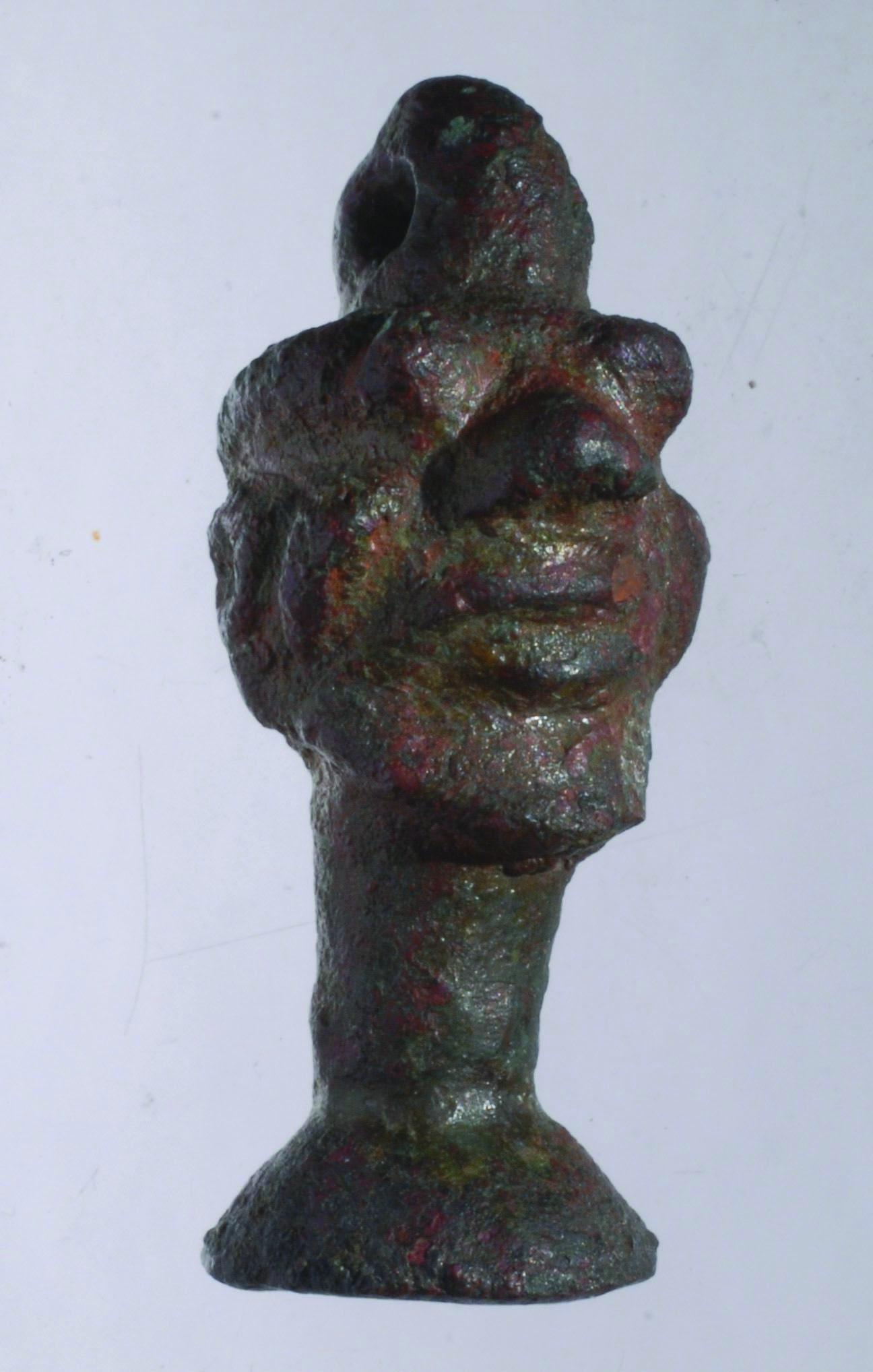 Bronze amulet of head with human and animal features and loop on top.