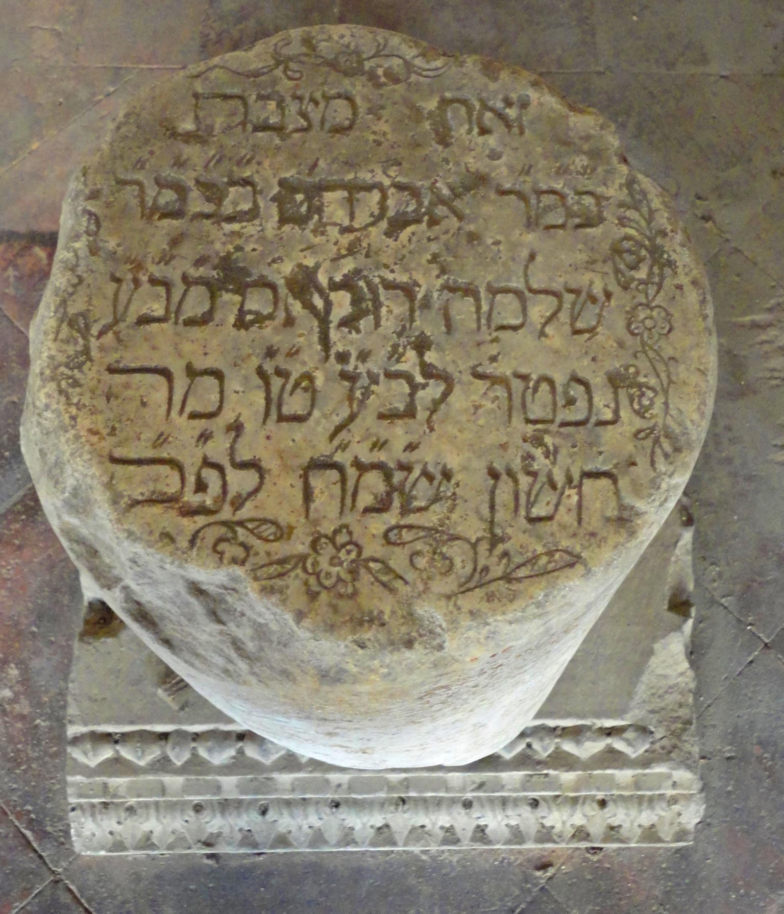 View from top of cylindrical tombstone with Hebrew on top and decorative base. 