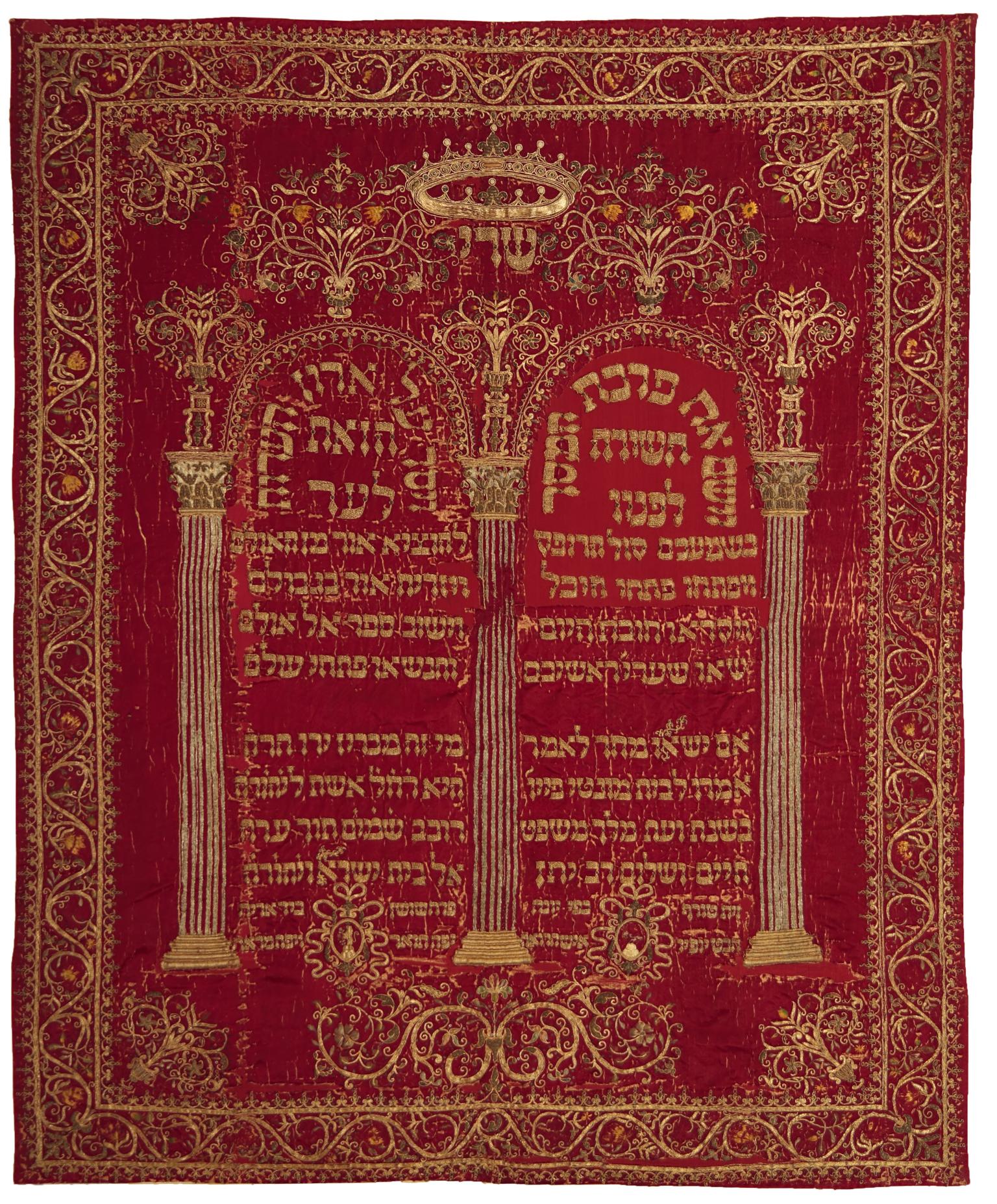 Cloth embroidered with Hebrew writing under columned archway and surrounded by decorative border. 