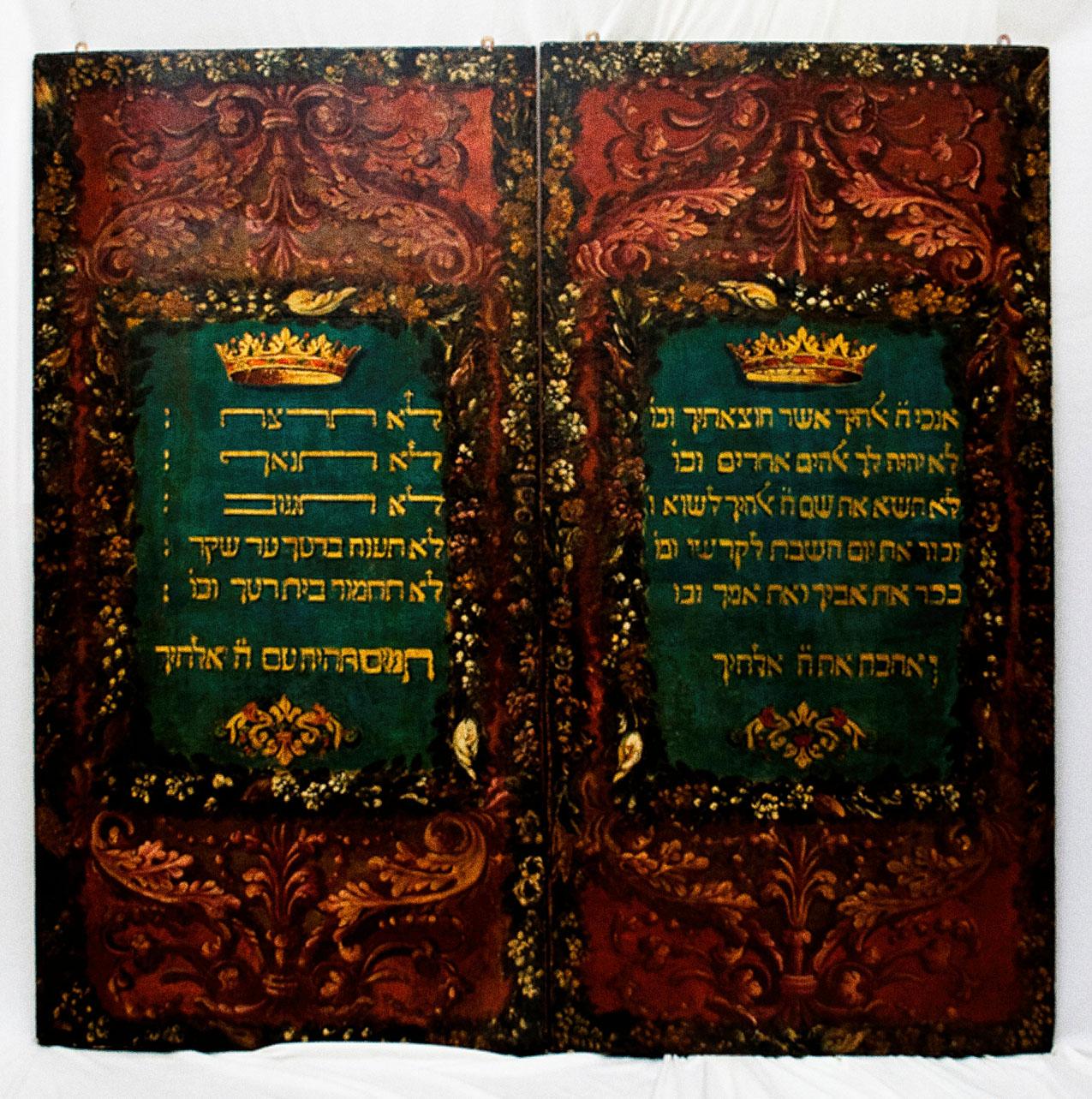 Carved double doors with Hebrew writing on left and right, with crowns above and floral decoration below, surrounded by carved decorative motifs. 