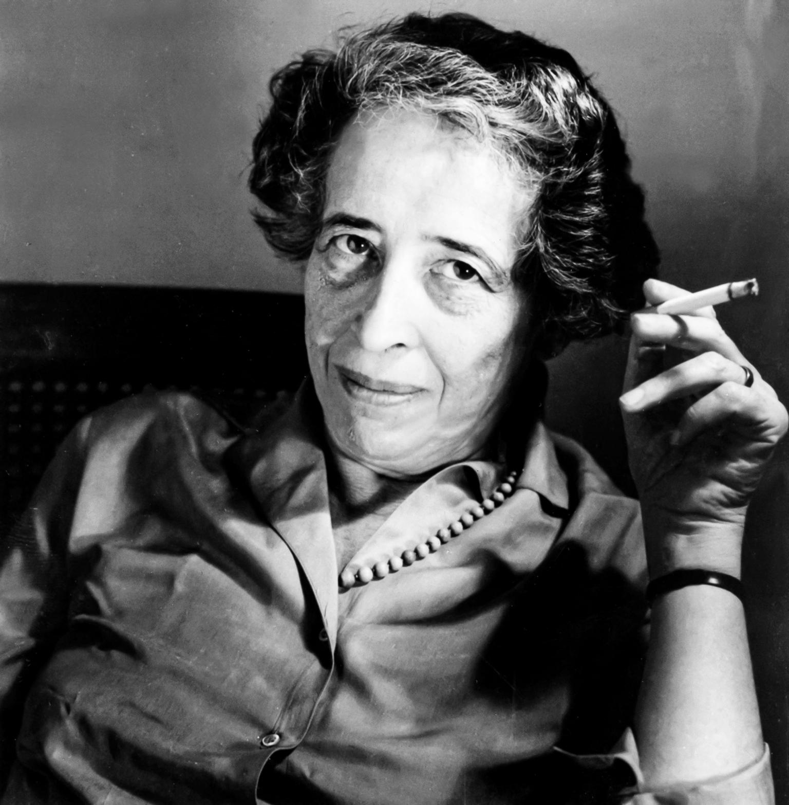 Portrait photograph of a woman looking at the camera and holding up a cigarette in her left hand.