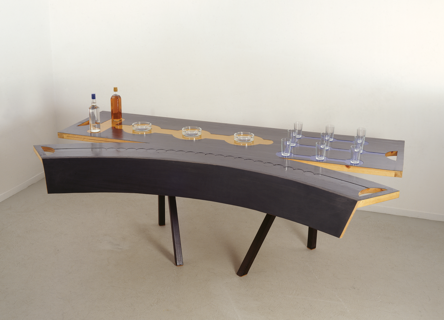 Sculpture of a cracked table with set of drinking glasses and glass ashtrays on it. 