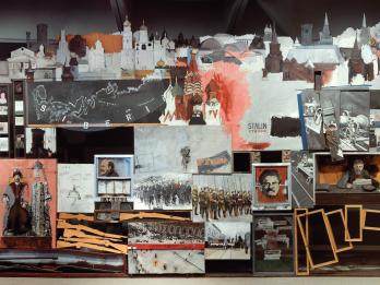 Mixed media installation featuring photos, images, frames, and cut-outs depicting soldiers in a row, profiles of male faces, maps, and informational text. 