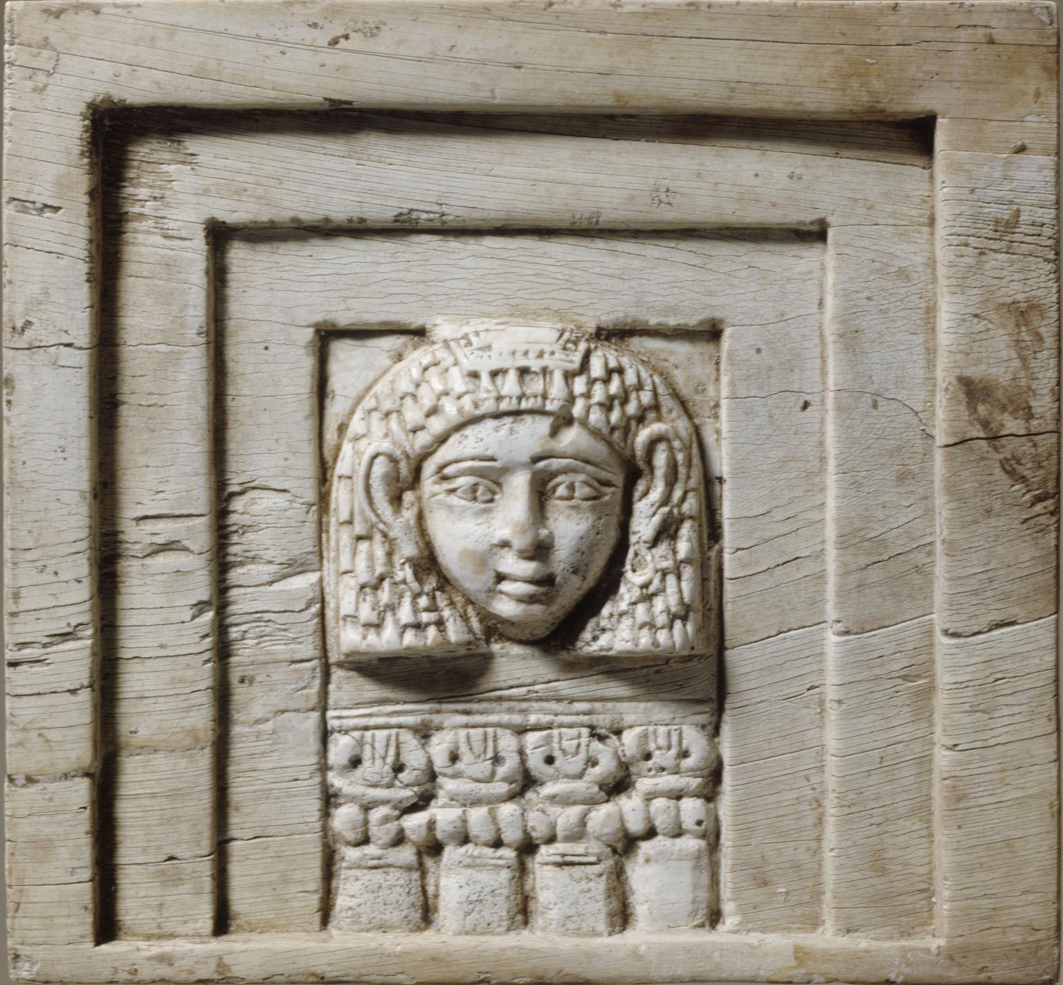 Rectangular relief of face framed in rectangular layers and four small columns below.